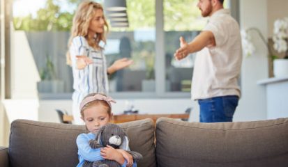 Kid feeling upset while parents argue in room. Couple arguing around child. Impact of family conflicts or divorce. Sad girl hugging teddybear