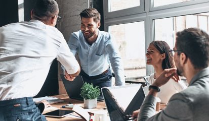 Young modern men in smart casual wear shaking hands and smiling while working in the creative office